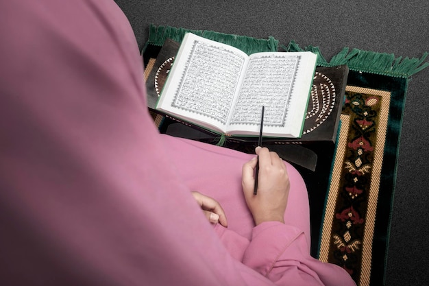 Muslim woman in a veil sitting on the prayer rug and reading the Quran