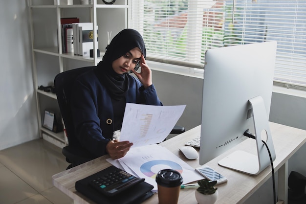 Muslim woman wearing hijab sitting on office chair, looking at the sheet with serious thinking about