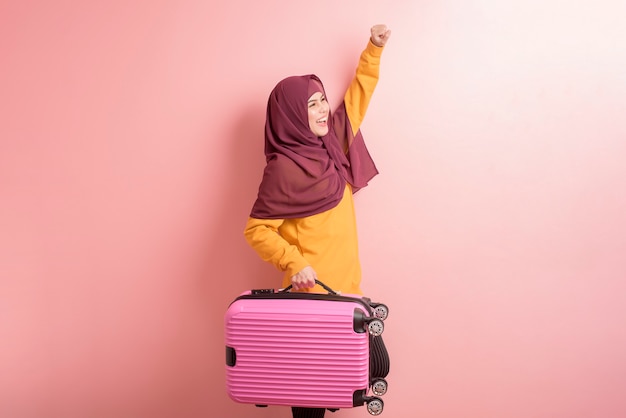 Muslim woman with hijab is holding luggage on pink background , people travel concept