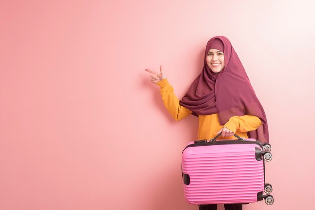 Muslim woman with hijab is holding luggage on pink background , people travel concept