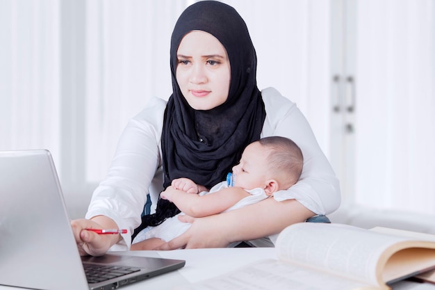 Muslim woman work while holding her baby at home