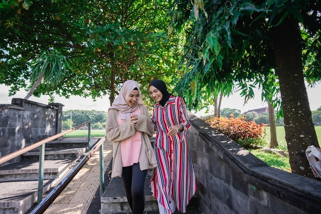 Muslim women in hijabs outdoors on sunny day with friend happy and laugh while walking outdoor