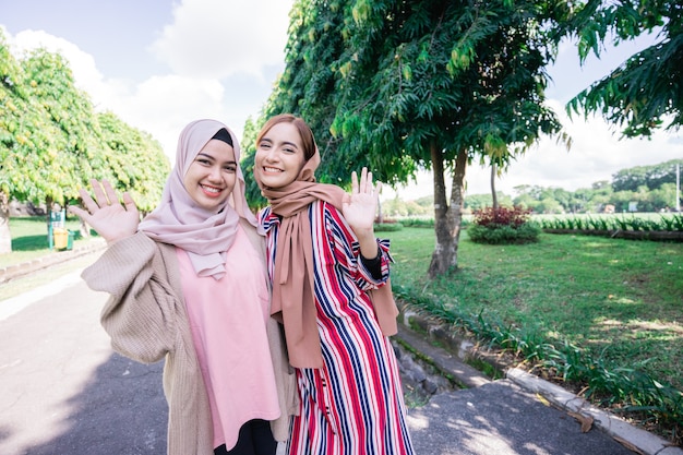 Muslim women in hijabs outdoors on sunny day with friend happy wave their hand