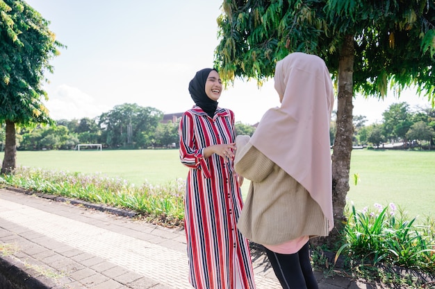 Muslim women in hijabs outdoors on sunny day with friend happy