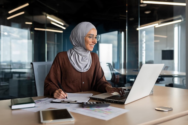 Muslim young woman in hijab programmer developer working in office behind notebook and with