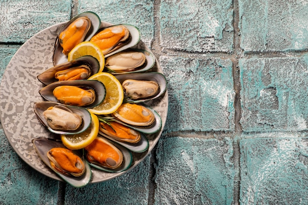 Mussel meat in a half of a shell with lemon on a blue tile background