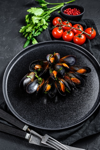 Mussels in tomato sauce decorated with parsley and cherry tomatoes. Black background. Top view