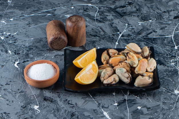 Mussels without shell and sliced lemons on a platter, on the marble surface.