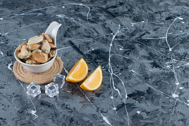 Mussels without shell in a spoon on a trivet next to sliced lemon, on the marble background. 