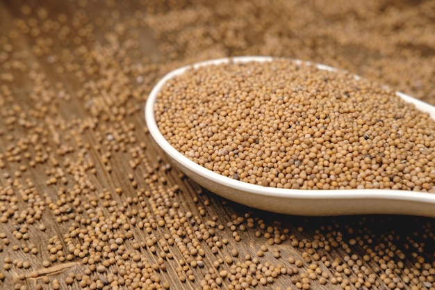 Mustard seeds in a spoon on the right on a wooden background