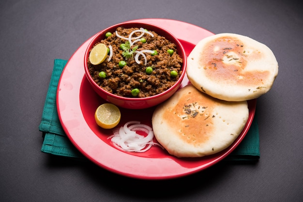 Mutton Kheema Pav OR Indian Spicy Minced Meat served with bread OR kulcha, garnished with green peas. Moody background. Selective focus