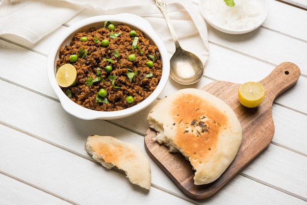 Mutton Kheema Pav OR Indian Spicy Minced Meat served with bread OR kulcha, garnished with green peas. Moody background. Selective focus