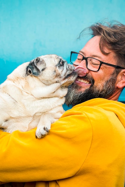 My best friend dog concept with funny scene adult man with beard and pug dog kissing him on the face people and animals have fun and love together in friendship