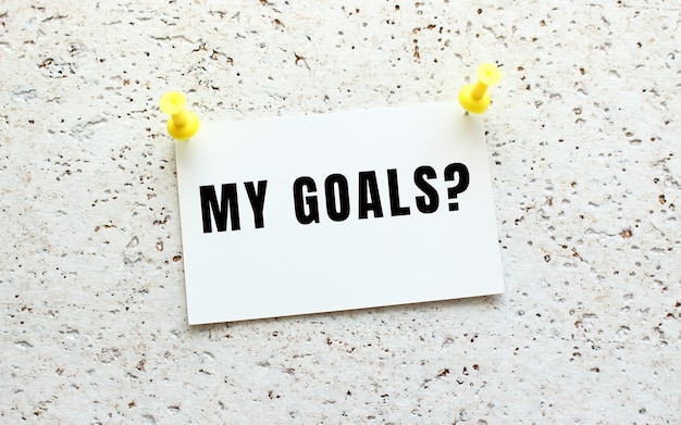 MY GOALS is written on a card attached to a white textured wall with a button. Office reminder.