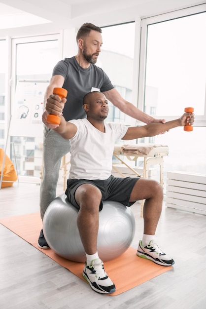 My job. Nice professional coach standing behind his client while having a workout with him