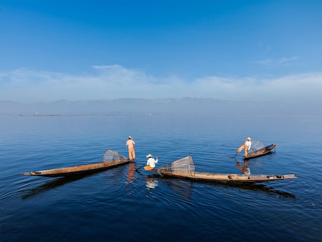 Myanmar travel attraction landmark Traditional Burmese fishermen with fishing nets on boats at Inle lake in Myanmar famous for their distinctive one legged rowing style