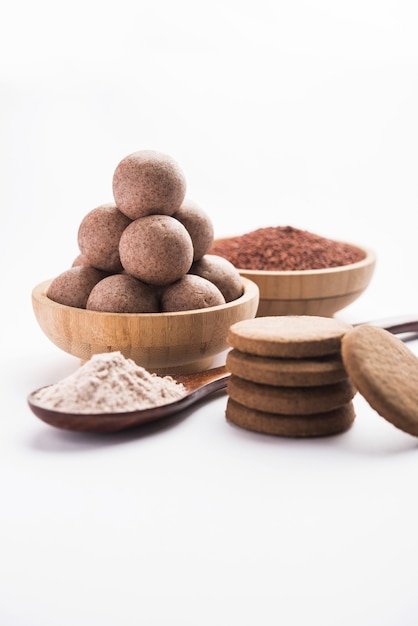 Nachni or Ragi laddu and biscuits or cookies made using  finger millet, sugar and ghee. It's a healthy food from India. Served in a bowl or plate with raw whole and powder