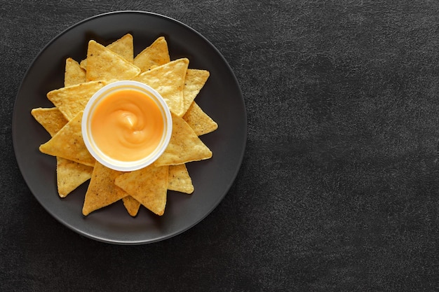 Nachos on grey plate and cheese salsa on dark background top view space to copy text