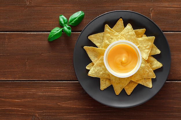 Nachos with cheese salsa leaf of green basil on plate on wooden brown plank tabletop background top view space to copy textxA