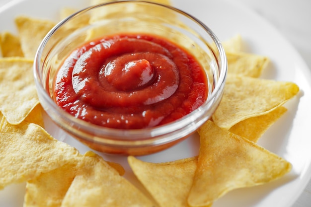 Nachos with tomato salsa on white plate closeup selective focus