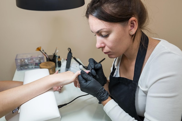 Nail care concept Manicurist makes a manicure to a client girl in a beauty salon