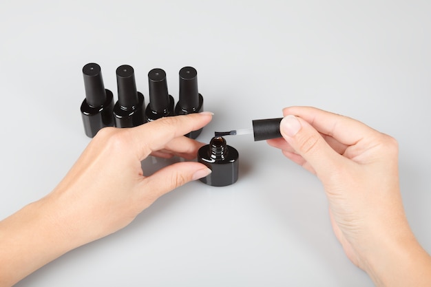 Nail care. woman opens a jar of lacquer on grey