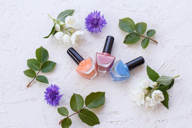 Nail polish bottles with jasmine flowers and green leaves on white background. Top view.