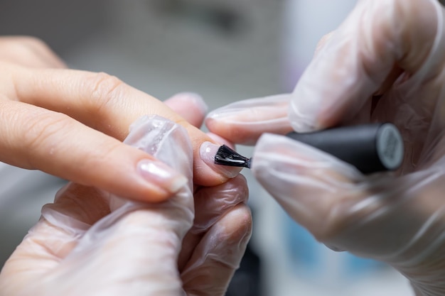 The nail service master does a manicure holds his finger and applies a transparent gel polish to protect the nail