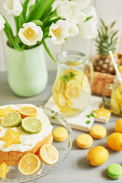 Naked cake with lemons and limes, lemonade, fruits, sweet macarons and tulip flowers