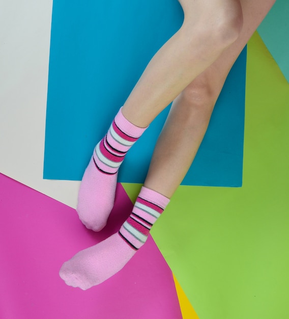 Naked female feet in socks posing on a multi-colored paper wall. Top view.