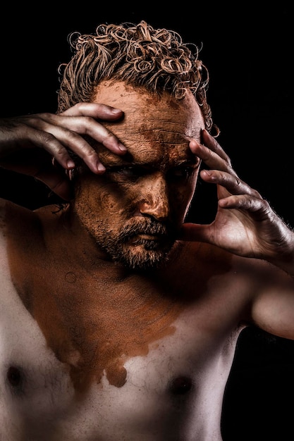 naked man with his face covered in clay, thinking