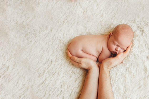 Naked newborn baby lying on the hands of parents on a white .