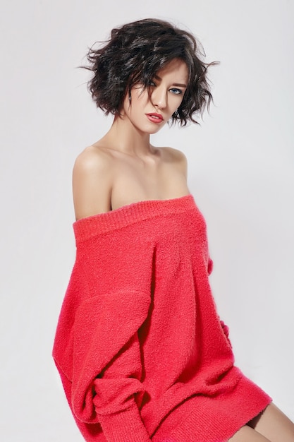 Naked sexy woman with short hair. Girl posing in a red sweater on a white background. Perfect clean skin, sexy Nude body of brunette woman. Skin rejuvenation and hydration