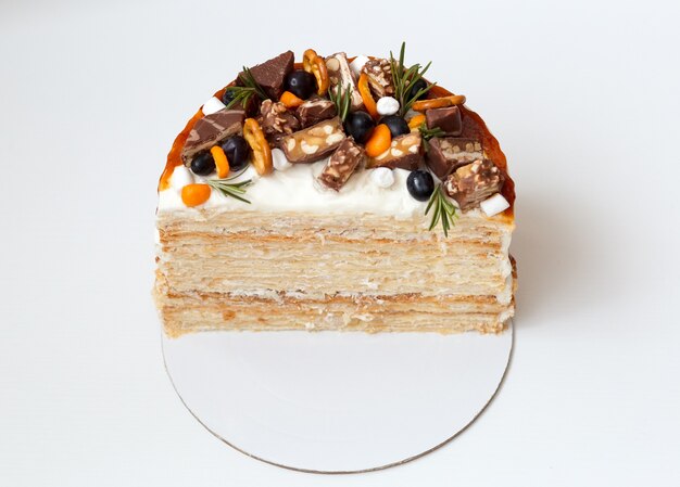 Napoleon cake in cut, a piece of cake decorated with berries, chocolate and sweets on a white surface