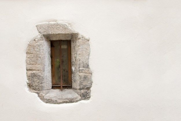 Narrow little dirty window with a brown frame on a background of white stone wall