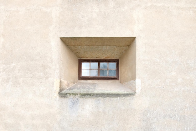 Narrow little window with brown frame on a background of white stone wall