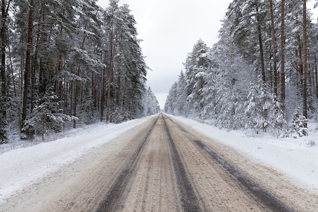 Narrow snow-covered winter road for car traffic, cloudy sky on the road, snow on the road melts from car traffic