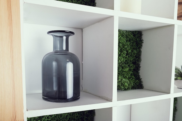 Narrowmouthed dark gray glass vase on a square white bookshelf