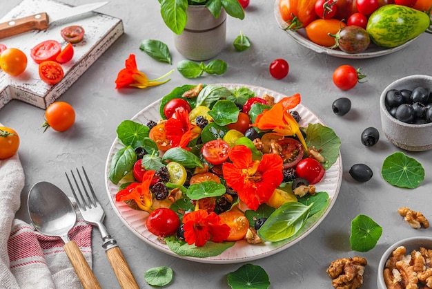 Nasturtium salad with vegetables olives nuts and raisins on gray concrete background with cutlery Healthy food