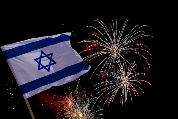 National Israel flag blowing and festive fireworks on black Independence Day Concept of celebration patriotism and Yom Haatzmaut Holiday background with Israeli flag and firework display at night