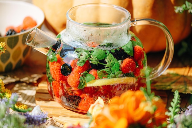 Natural aromatic fruit tea in a transparent teapot and in a cup among berries and flowers warming aromatic tea with a deep aroma of berries and wildflowers