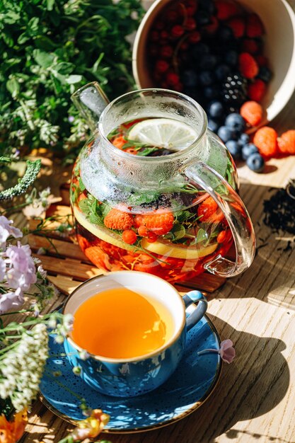 Natural aromatic fruit tea in a transparent teapot and in a cup among berries and flowers warming aromatic tea with a deep aroma of berries and wildflowers