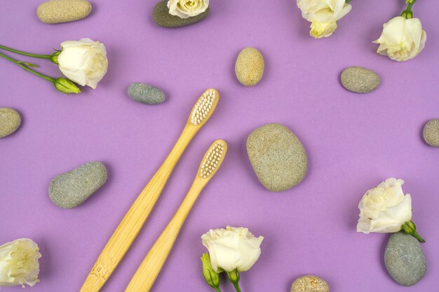 Natural bamboo toothbrushes with pebbles and flowers on a purple background. No waste concept, no plastic