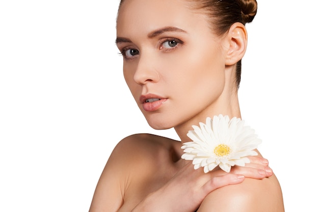 Natural beauty. Beautiful young shirtless woman holding flower on her shoulder and looking at camera while isolated on white background