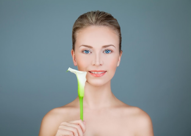 Natural Beauty. Healthy Woman with Lily Flower Smiling on Blue Background