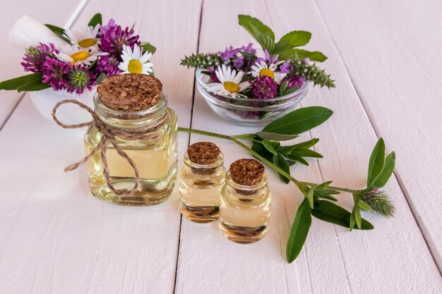 Natural cosmetic in glass bottles on a white wooden table chamomile flowers clover mint in bowls natural organic care