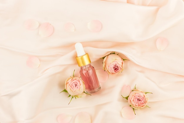 Natural cosmetic product. rose petal oil in a glass flamon with a dropper on a pastel textile background with rose buds.