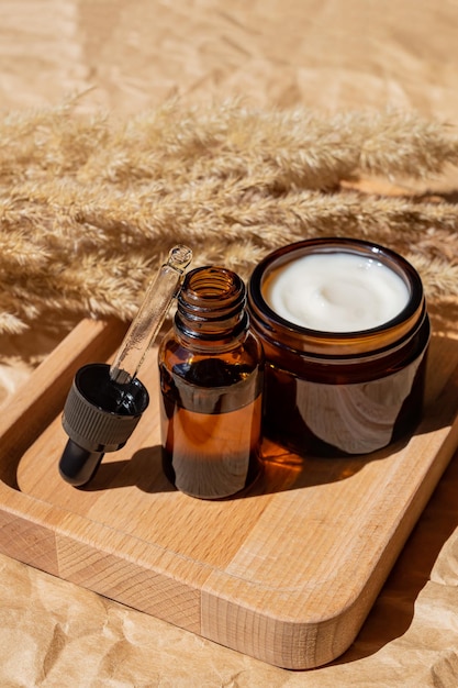 Natural cosmetics in amber glass packaging on wooden tray on brown background with dried reeds flowers SPA organic beauty products set Skin care concept