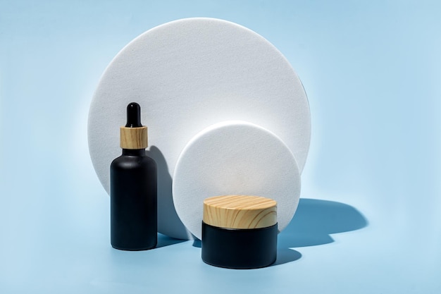 Natural cosmetics in bamboo and black glass packaging on blue background with white round podium SPA organic beauty products set Skin care concept