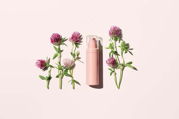 Natural cosmetics product pink spray bottle and field clover flowers on pale pink face or body cream